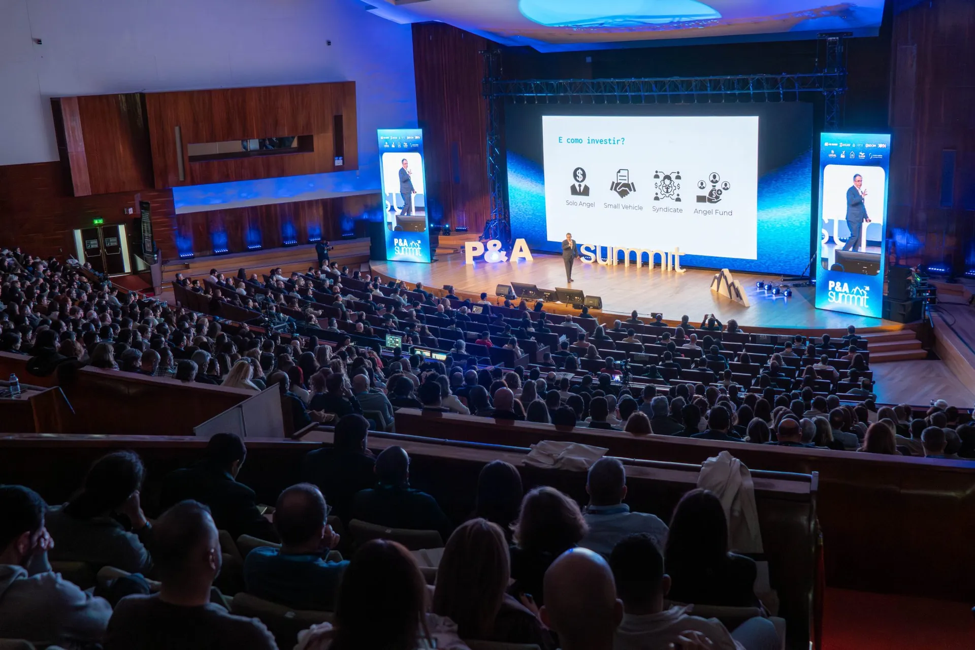 Plateia cheia na Aula Magna, em Lisboa, durante o P&A Summit 2026, com o palco e os ecrãs do evento ao fundo